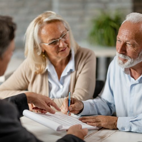Mature couple having a meeting with bank manager and signing lease agreement in the office. Focus is mature man.